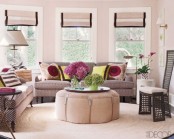 a pastel pink living room with touches of brown and black for a contrast, with blooms and colorful printed pillows, a tall chair and lovely shades