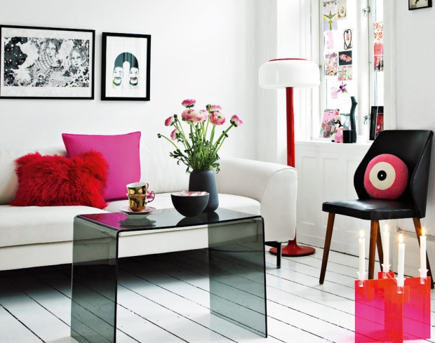 a modern and contrasting feminine living room in white, with a black acrylic table and chair, black and white art and touches of hot pink and candles