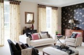 a bold and chic living room with a dark floral accent wall, white furniture and a brown chair, neutral floral curtains and pink pillows
