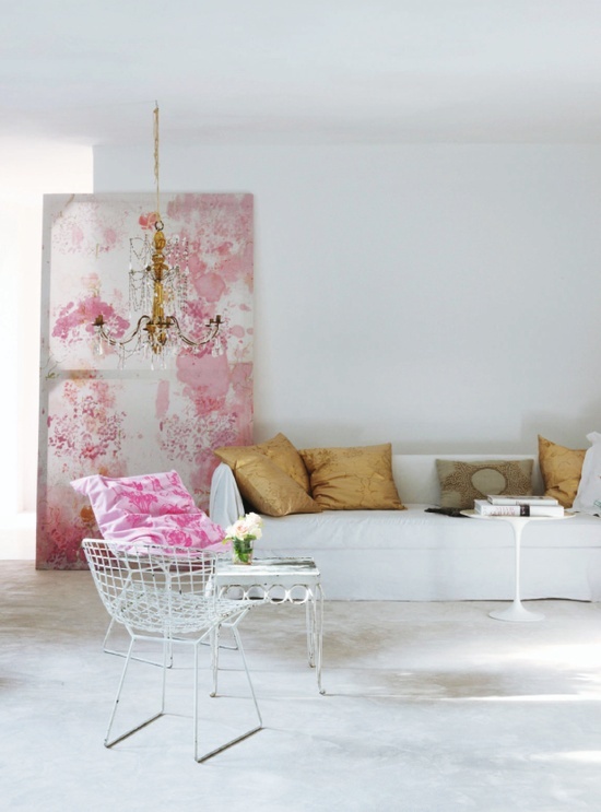 a chic and stylish feminine living room in neutrals, with a white sofa, gold pillows, a chair with a pink sofa and a shabby chic artwork in pink plus a refined chandelier