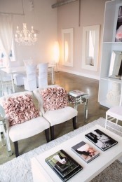 a refined neutral feminine living room with white chairs and pink pillows, a bookcase and a low coffee table plus pendant lamps