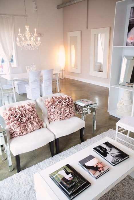 a refined neutral feminine living room with white chairs and pink pillows, a bookcase and a low coffee table plus pendant lamps