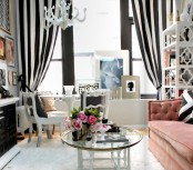 a catchy and contrasting feminine living room in black and white, with striped curtains, a pink sofa, black and white furniture and a refined crystal chandelier