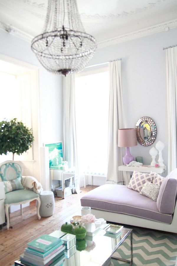 a delicate neutral and pastel living room with lilac walls, a lilac daybed, a mint green chair and some artworks, a crystal chandelier