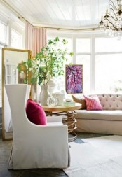 a lovely feminine living room with a neutral sofa and chair, a large gold coffee table, greenery and pink chairs is amazing