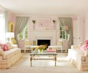 a stylish neutral living room with a fireplace, neutral sofas, a glass coffee table, green curtains, pink printed pillows