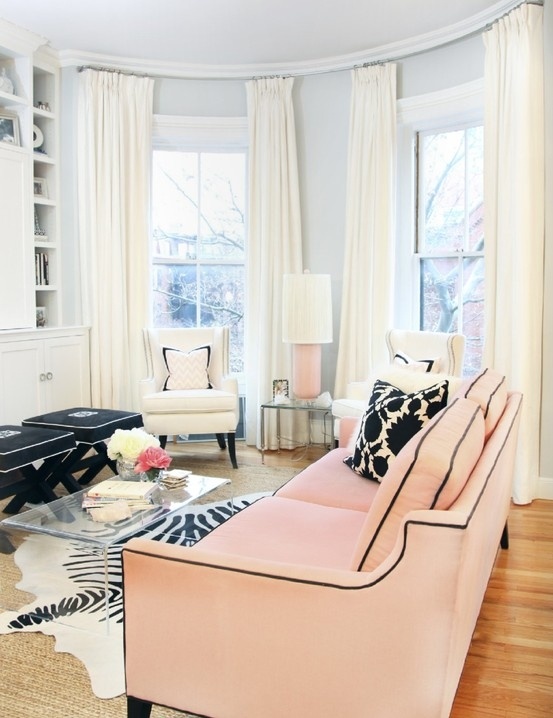 an elegant feminine living room with a pink sofa, white chairs, black stools and pillows, a glass chair and an animal printed rug
