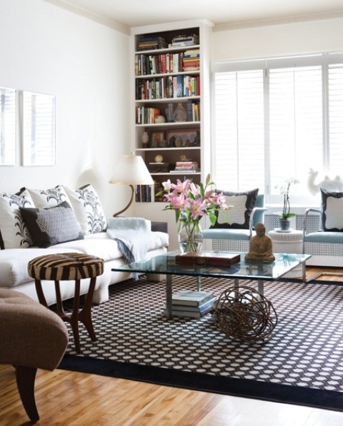 a sophisticated and contrasting living room with built in bookcases, a large sofa and blue chairs, a glass coffee table and a striped stool plus printed pillows