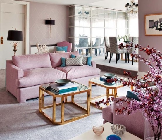 a cool feminine living room with mauve walls, pink sofas, a mirror wall, teal pillows and brass and glass coffee tables