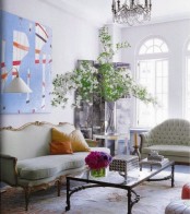 a fresh and airy living room with arched walls, vintage light green furniture, a glass coffee table, a bold artwork and a potted tree