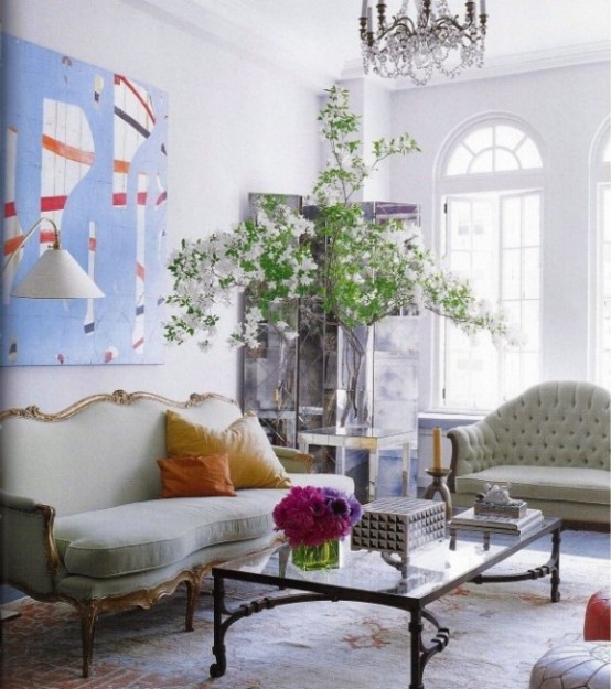 a fresh and airy living room with arched walls, vintage light green furniture, a glass coffee table, a bold artwork and a potted tree