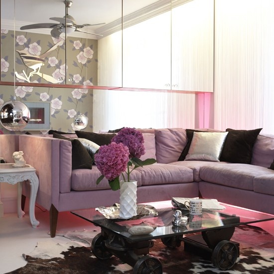 a glam feminine living room with a lilac corner sofa, a glass mirror wall, a glass coffee table and an animal print rug