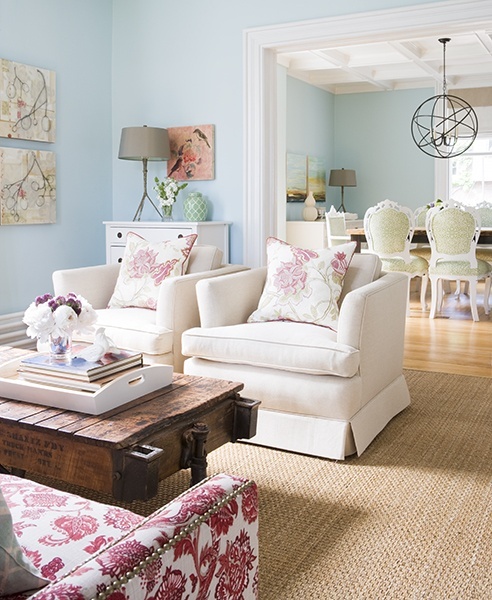 a lovely modern living room with feminine touches, a jute rug, a dark-stained wooden table, neutral chairs, a pink and white floral sofa and matching pillows