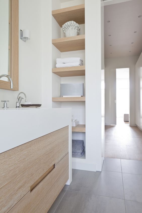 a contemporary bathroom in white and stained wood, wih a series of niche, a stained floating vanity, a mirror with a light-stained frame