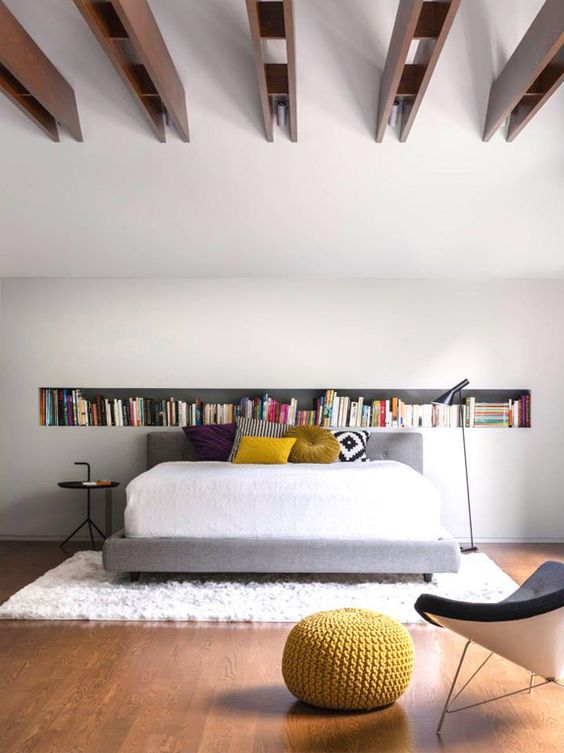 a contemporary bedroom with a long niche shelf, a bed with bold pillows, a black side table and black chair