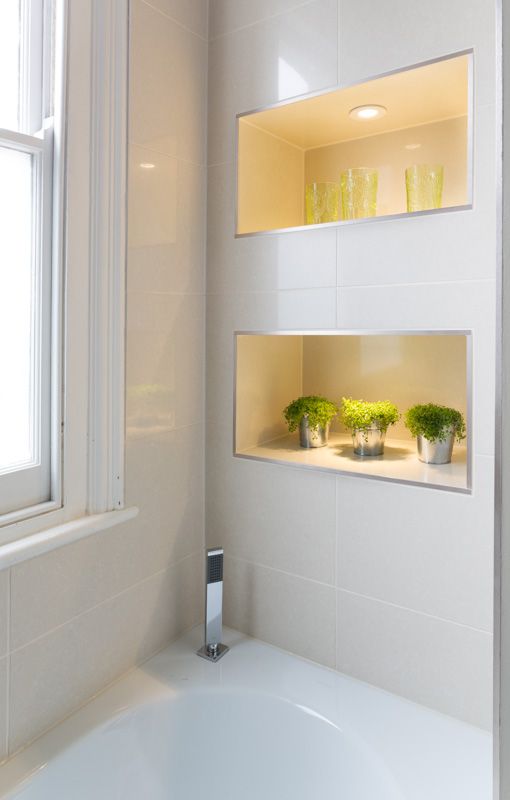 a contemporary bathroom with lit up niche shelves that feature storage and display space and add decorative value