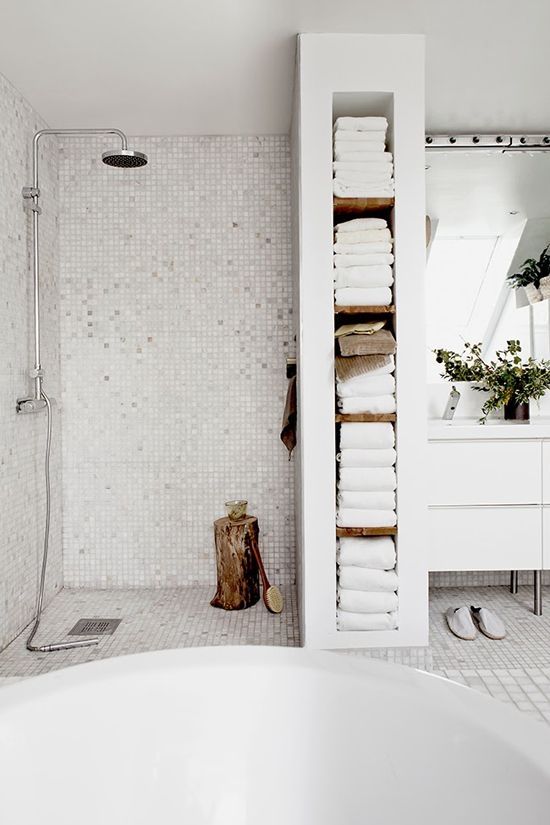 a contemporary neutral bathroom with a shower space and a space divider that provides niche shelves and towel storage