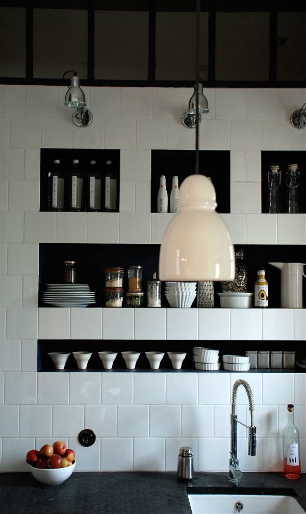 a creative black and white kitchen with square tiles and niche shelves that are used instead of upper cabinets for storing various tableware