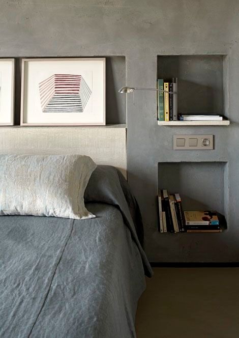 an industrial bedroom with concrete walls and niche shelves instead of nightstands, this is a great alternative to usual shelves and they look sleek