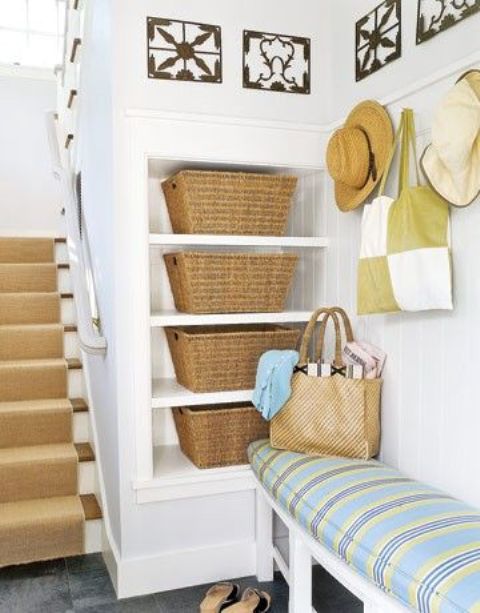 a cottage entryway with niche shelves and woven boxes plus an upholstered bench is a cozy and cute space with plenty of storage