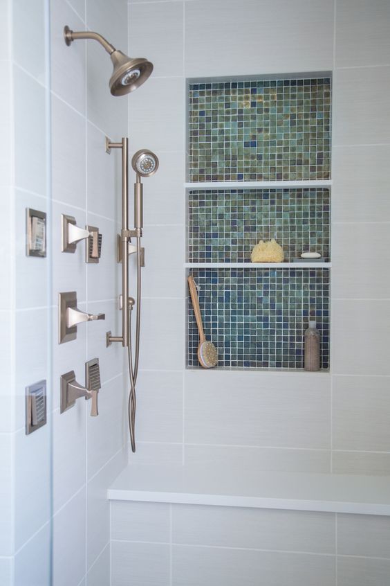 a neutral bathroom clad with tiles, with a niche shelf clad with green tiles, storing stuff for washing