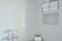 a white bathroom clad with glazed tiles, with sleek niche shelves that are used for storage and to save space
