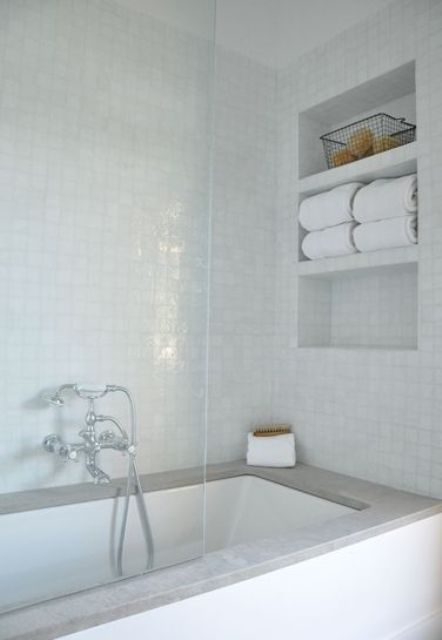 a white bathroom clad with glazed tiles, with sleek niche shelves that are used for storage and to save space