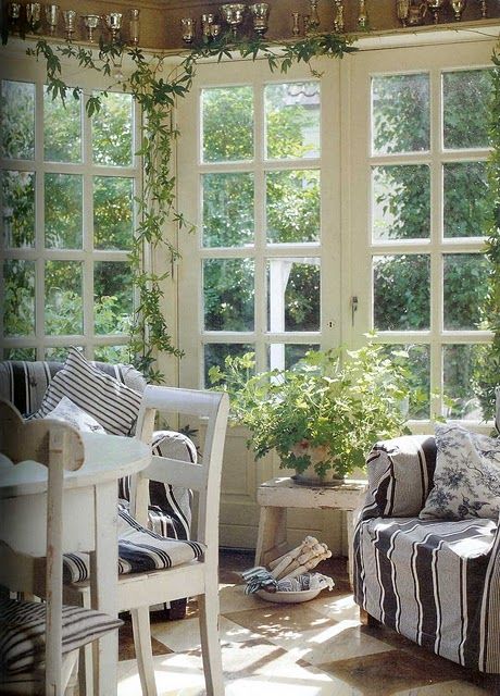 a vintage Scandinavian sunroom with striped black and white vintage furniture, potted greenery and lots of sunlight coming in