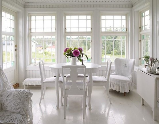 a white Nordic sunroom with white vintage furniture, white furniture covers, potted plants and flowers