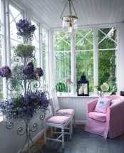 a vintage Scandinavian sunroom with white planks, a printed chair and stools, a vintage metal stand with lots of blooms