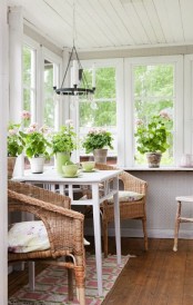 a Nordic sunroom with a white table and wicker chairs, potted greenery and blooms and a printed plant is amazing