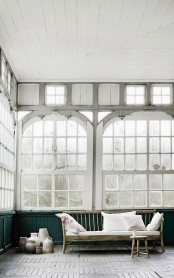 a vintage Scandinavian sunroom with green paneling and vintage window frames, bamboo furniture, vases and pots on the floor