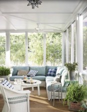 a Nordic sunroom with a light blue corner sofa, white chairs, pottted plants and printed pillows