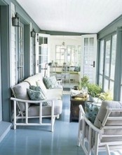 a light blue Scandinavian sunroom with white bamboo furniture, a stained chest, potted greenery and printed pillows