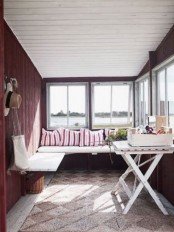 a burgundy Scandinavian sunroom with a built-in bench, a white trestle table and some striped pillows and some accessories