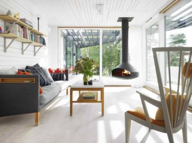 a white Scandinavian sunroom with a suspended hearth, Nordic furniture, open shelves, a low table and potted greenery