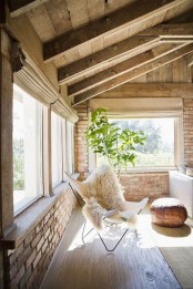 an airy Scandinavian sunroom with brick walls, wooden ceiling, a white sofa with pillows, a butterfly chair and a potted tree
