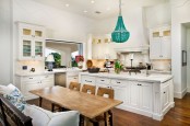 a white kitchen with shaker style cabinets, white stone countertops, lit up cabinets, a turquoise chandelier over the kitchen island