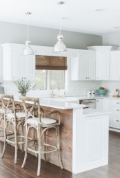 a white kitchen with white shaker cabinets, white tiles and white countertops, a kitchen island clad with wood and wooden stools for a beachy feel