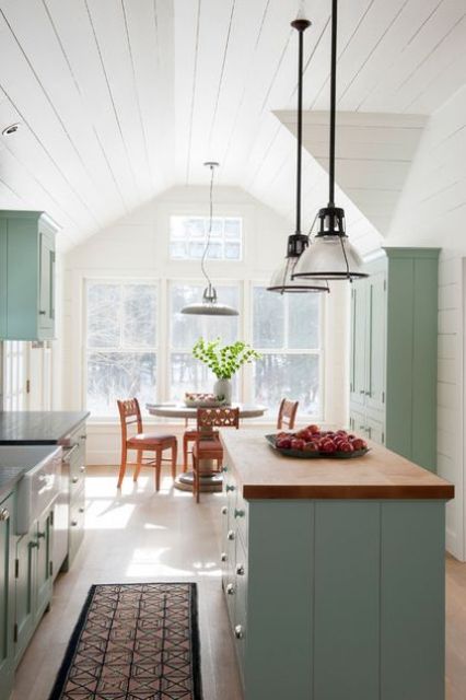 a light blue kitchen with shaker style cabinets, butcherblock countertops, glass pendant lamps and a neutral stained dining set by the window