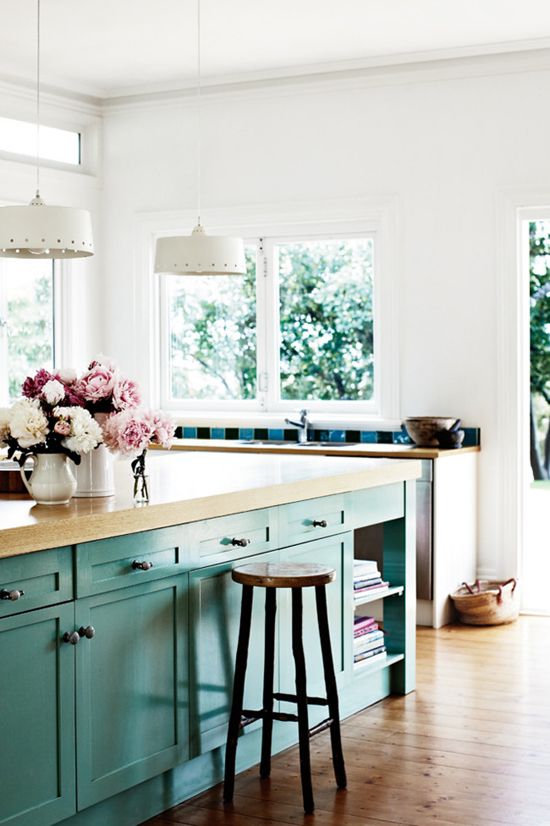 a pretty beach-inspired kitchen with a turquoise kitchen island with butcherblock countertops, a wooden stool, white kitchen cabinetry with butcherblock countertops and striped tiles