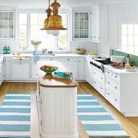 a pretty beach kitchen with white cabinets, a green tile and white beadboard backsplash, a bright turquoise striped rug