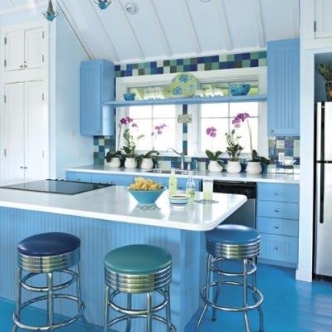 a small ocean blue kitchen with a blue floor, cabinets, a kitchen island, a multicolor tile backsplash and stools in various shades of green and blue