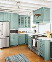 a beautiful turquoise kitchen with shaker style cabinets, white stone countertops and a whale decoration on the hood is a lovely space