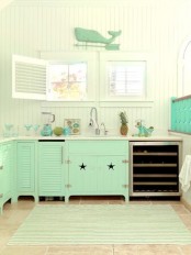 a bright beach kitchen with white beadboard walls, bright green cabinets, turquoise glasses and tableware and a green whale decoration