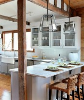 a relaxed beach kitchen with dove grey sleek cabinets, white stone coutnertops, wooden beams and lovely woven stools