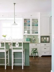 a white farmhouse kitchen with shaker style cabinets, a light green tile backsplash, a green kitchen with white stone countertops and white stools