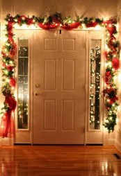 a bright Christmas garland of evergreens, red ribbon and lights is a cathcy decor idea for the holidays, cover the doorway with it