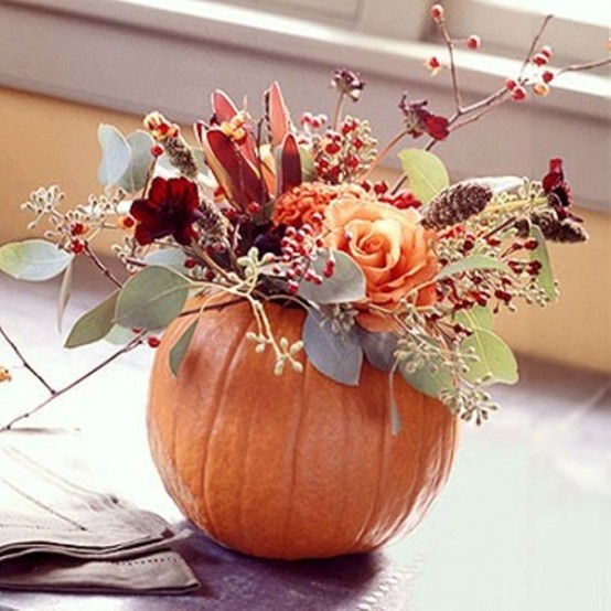 a bright fall pumpkin with burgundy and orange blooms and dark and usual greenery is a cool fall centerpiece