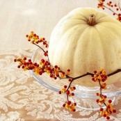 a glass plate with a white pumpkin and berry branches is a nice vintage-inspired fall centerpiece idea